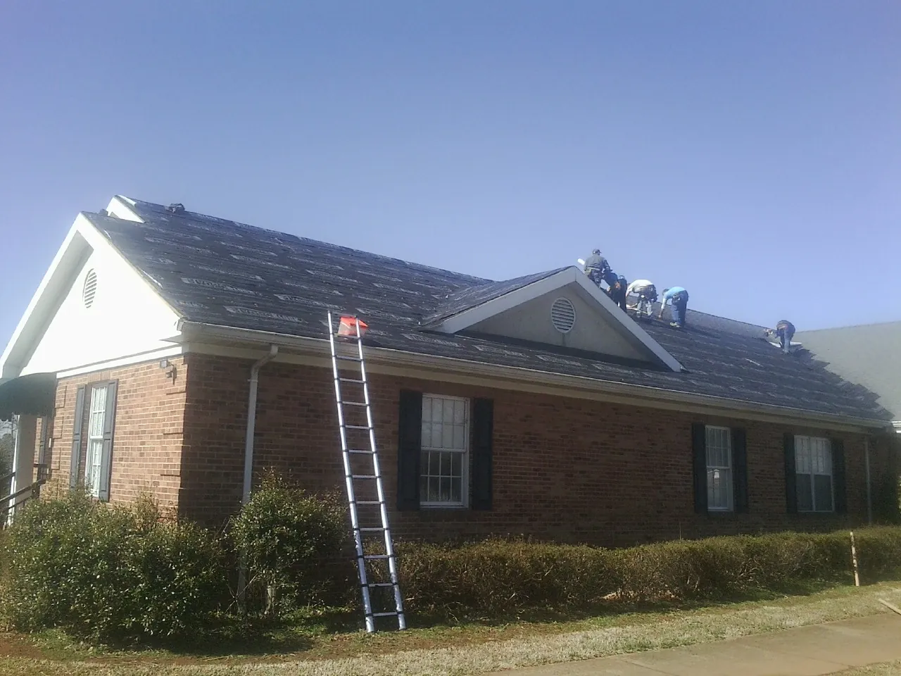 Crew tearing shingles off a brick ranch roof with a ladder set — Metal Roof Repair work by our crew in Westwood