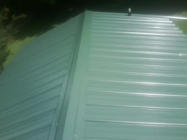 New green metal panels meeting at the ridge of a roof — Flat Roof Repair work by our crew in Westwood