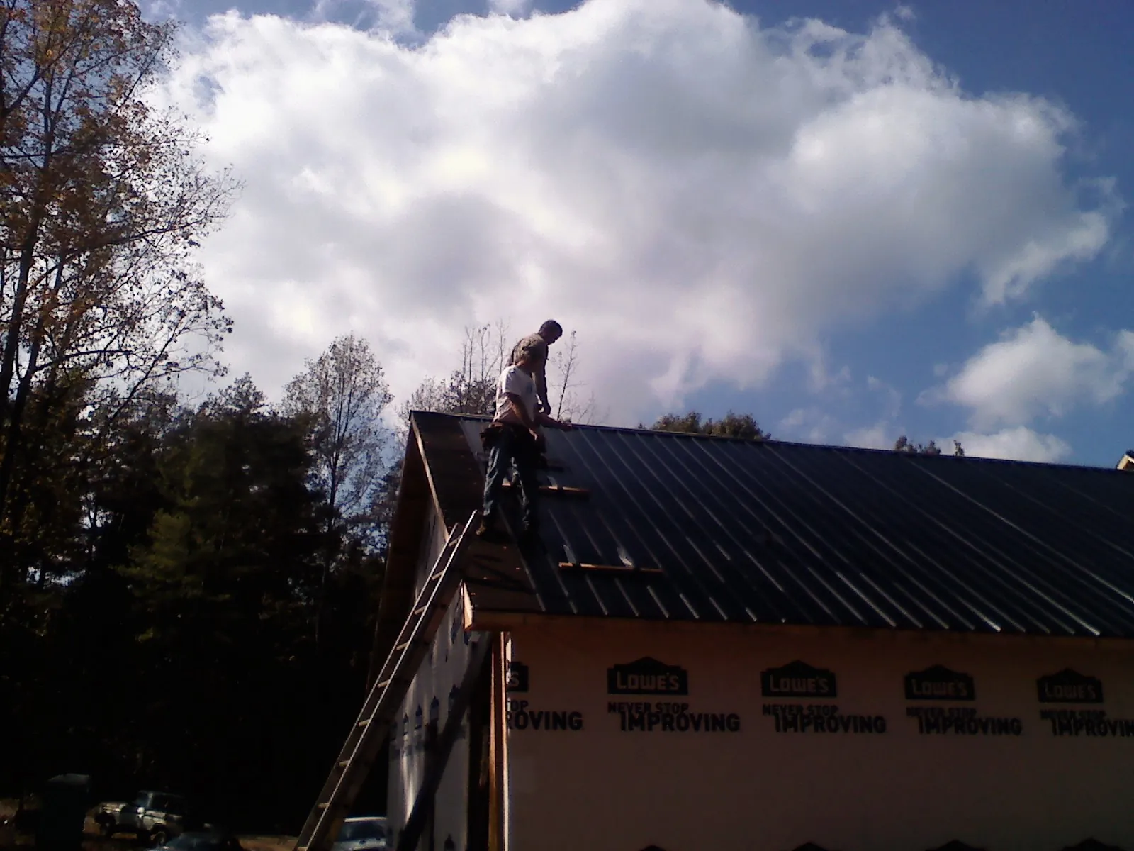 Roofer fastening dark metal panels high against a cloudy sky, from a Roof Inspection job in Westwood